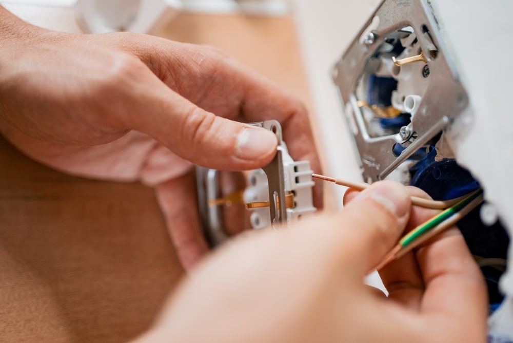 Installation de prise électrique par un électricien pro Mains d'un électricien raccordant des fils de cuivre à une prise électrique murale lors de travaux d'électricité.