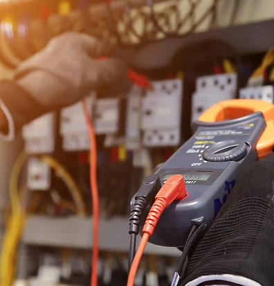 Électricien testant un tableau électrique avec une pince ampèremétrique de précision pour la maintenance.