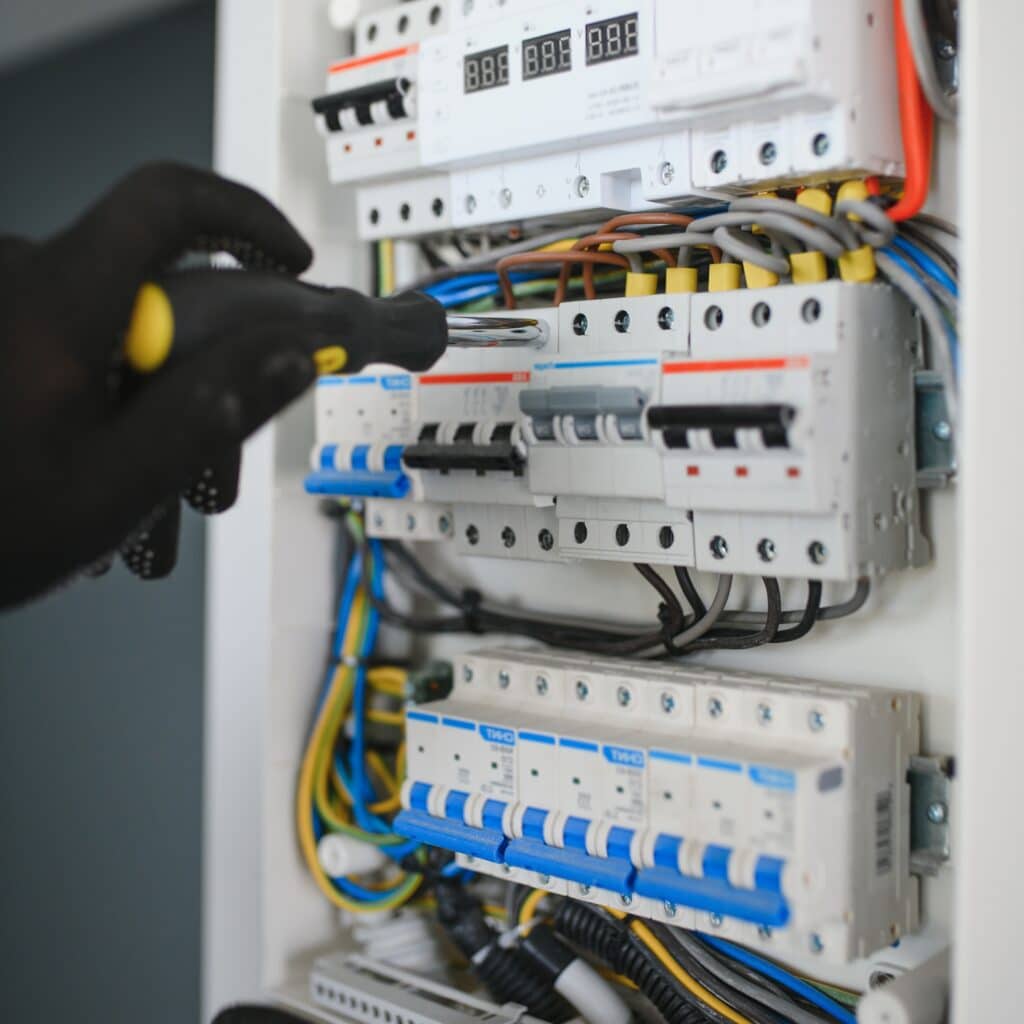 Installation et maintenance d'un tableau électrique Électricien ganté serrant une vis sur un disjoncteur dans un tableau électrique moderne avec câblage apparent.