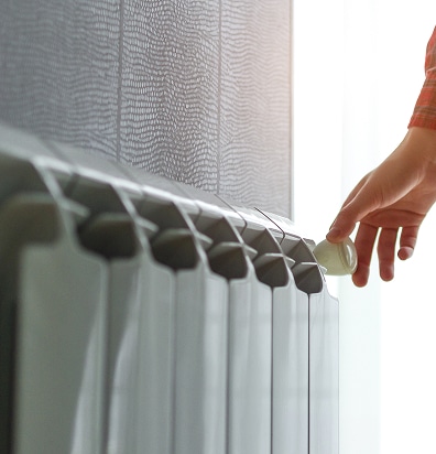 Main ajustant la valve thermostatique d'un radiateur blanc pour réguler le chauffage intérieur.