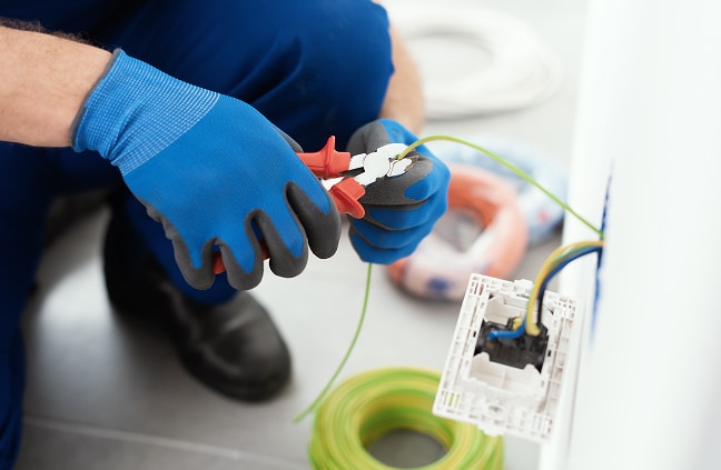 Installation Électrique : Travaux de Raccordement Professionnel Électricien utilisant une pince coupante pour dénuder un fil de terre près d'une installation électrique murale.